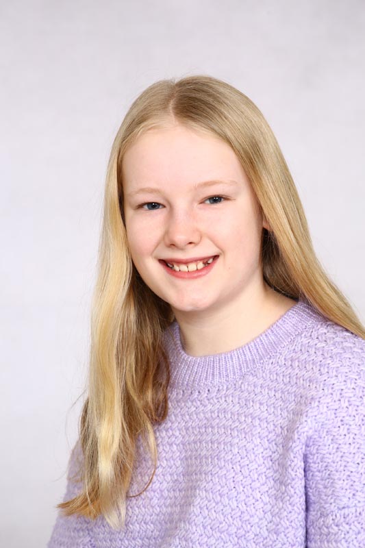 A young girl smiles while wearing a light purple jumper