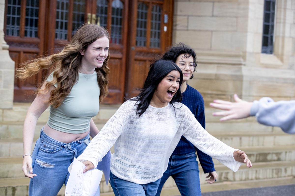 Three students running towards their friend