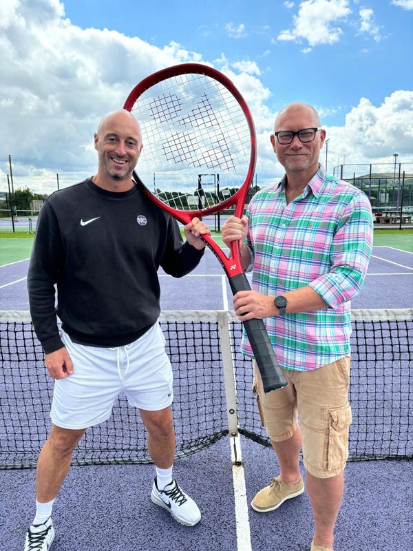 The Headmaster of Bradford Grammar School and the Founder of Skipton Tennis Centre holding a large tennis racket, stood on a tennis court.