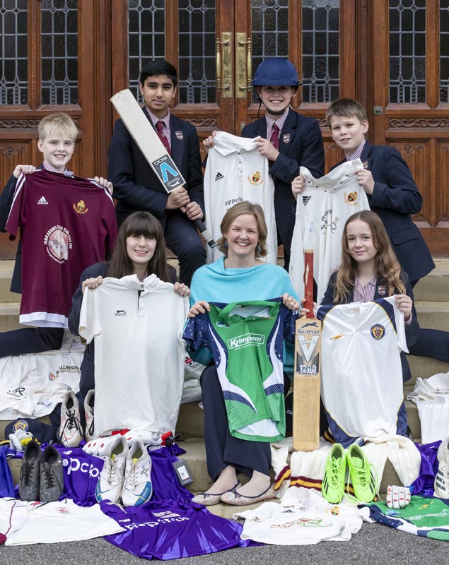 Teacher and pupils sat on stairs holding up sports kit donations