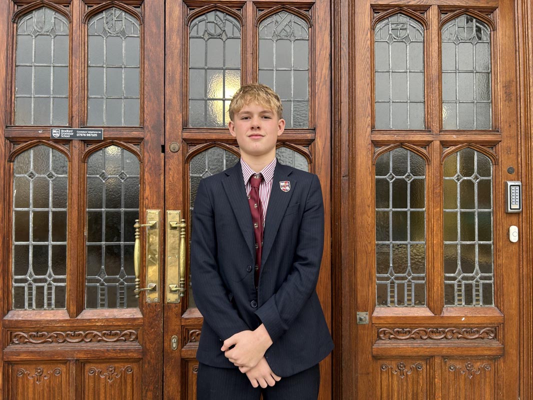 Bradford Grammar School pupil stood with his arms crossed outside a wooden door.