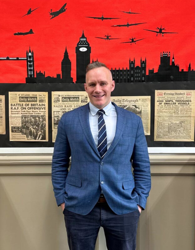 Bradford Grammar History teacher stood smiling infront of an educational history display in a classroom.